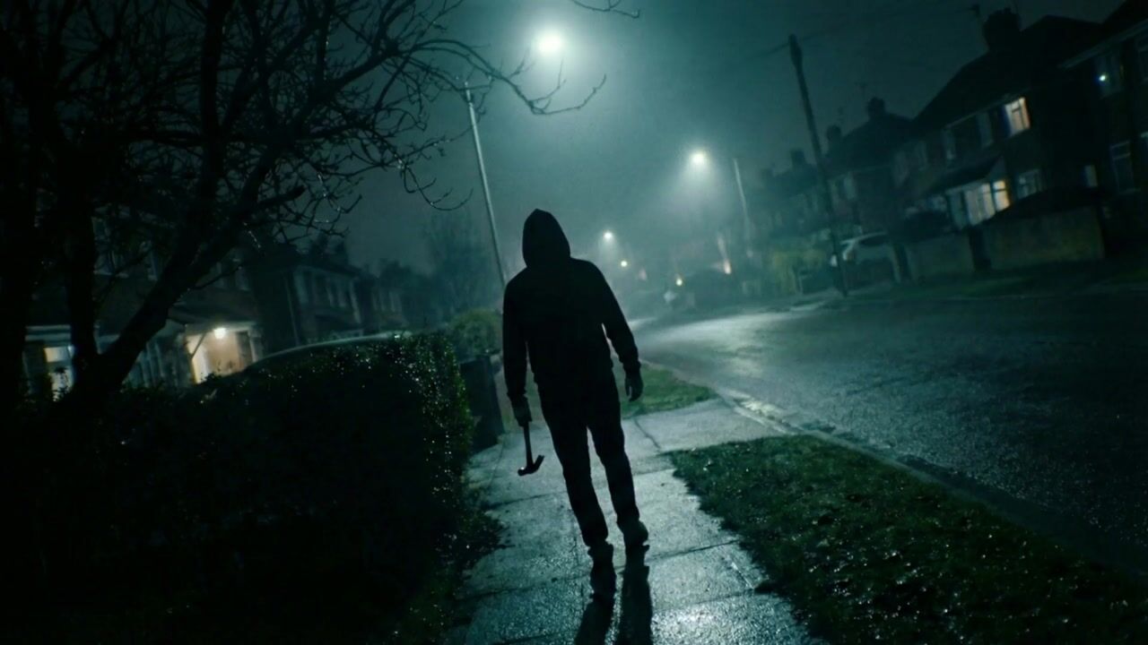 Hooded figure walking down a wet suburban street at night